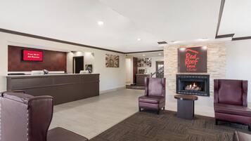 Um saguão de hotel com balcão de recepção, sinalização de Wi-Fi gratuito, placa Red Roof Inn, poltronas de couro e lareira.