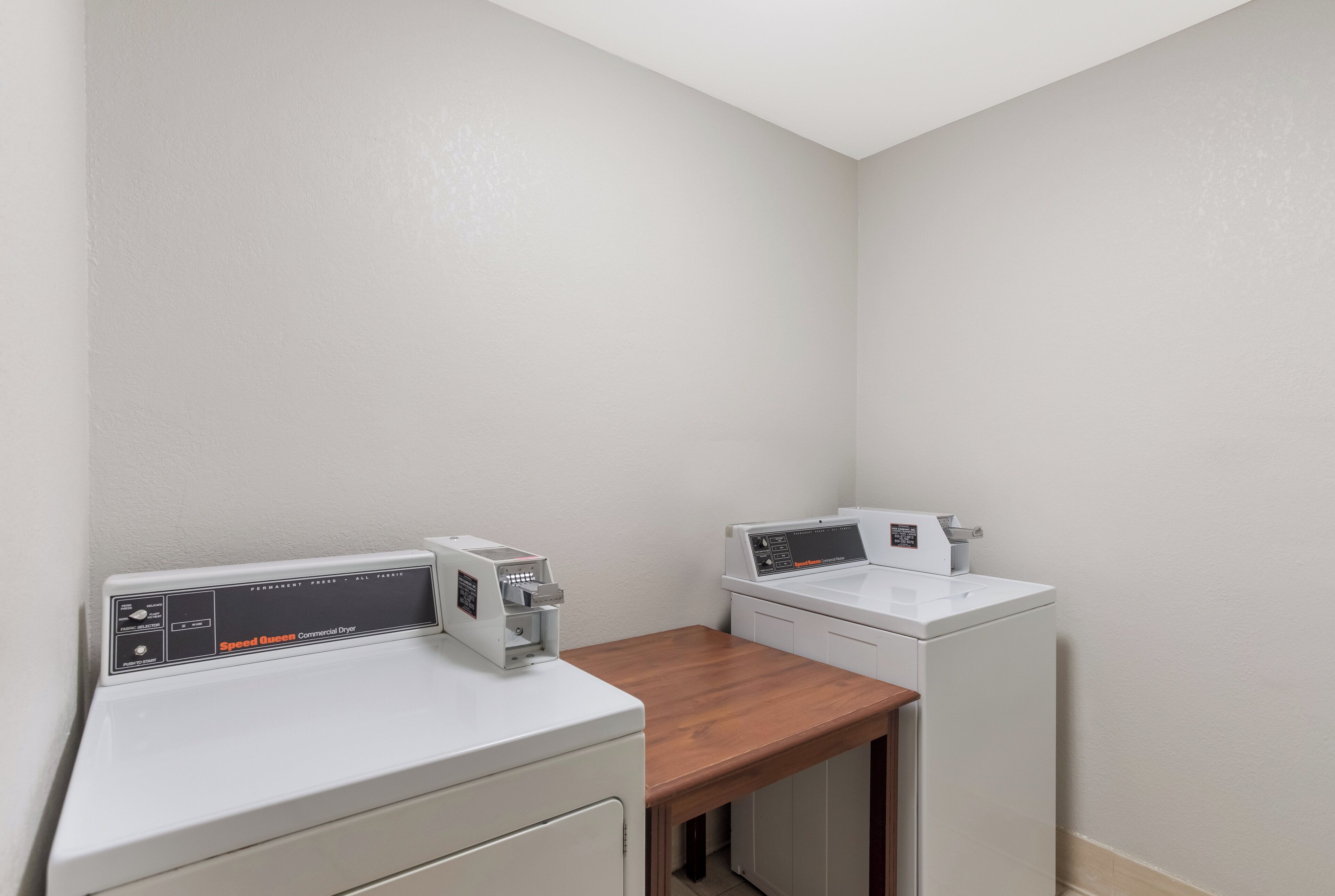 A laundry area with two white washing machines and a dryer, a wooden counter, and a white wall.