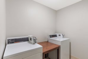 Un área de lavandería con dos lavadoras blancas y una secadora, una encimera de madera y una pared blanca.