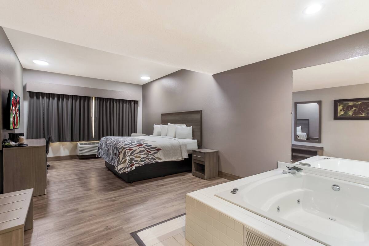 A modern hotel room with a large bed, a separate bathroom with a bathtub, a desk, and a TV.