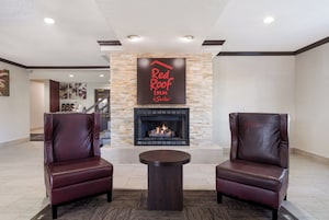 Vestíbulo de Red Roof Inn & Suites con chimenea de piedra, sillones de cuero y una pequeña mesa redonda.