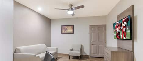 Una habitación con ventilador de techo, un televisor montado en la pared, una puerta y un pequeño cuadro enmarcado.