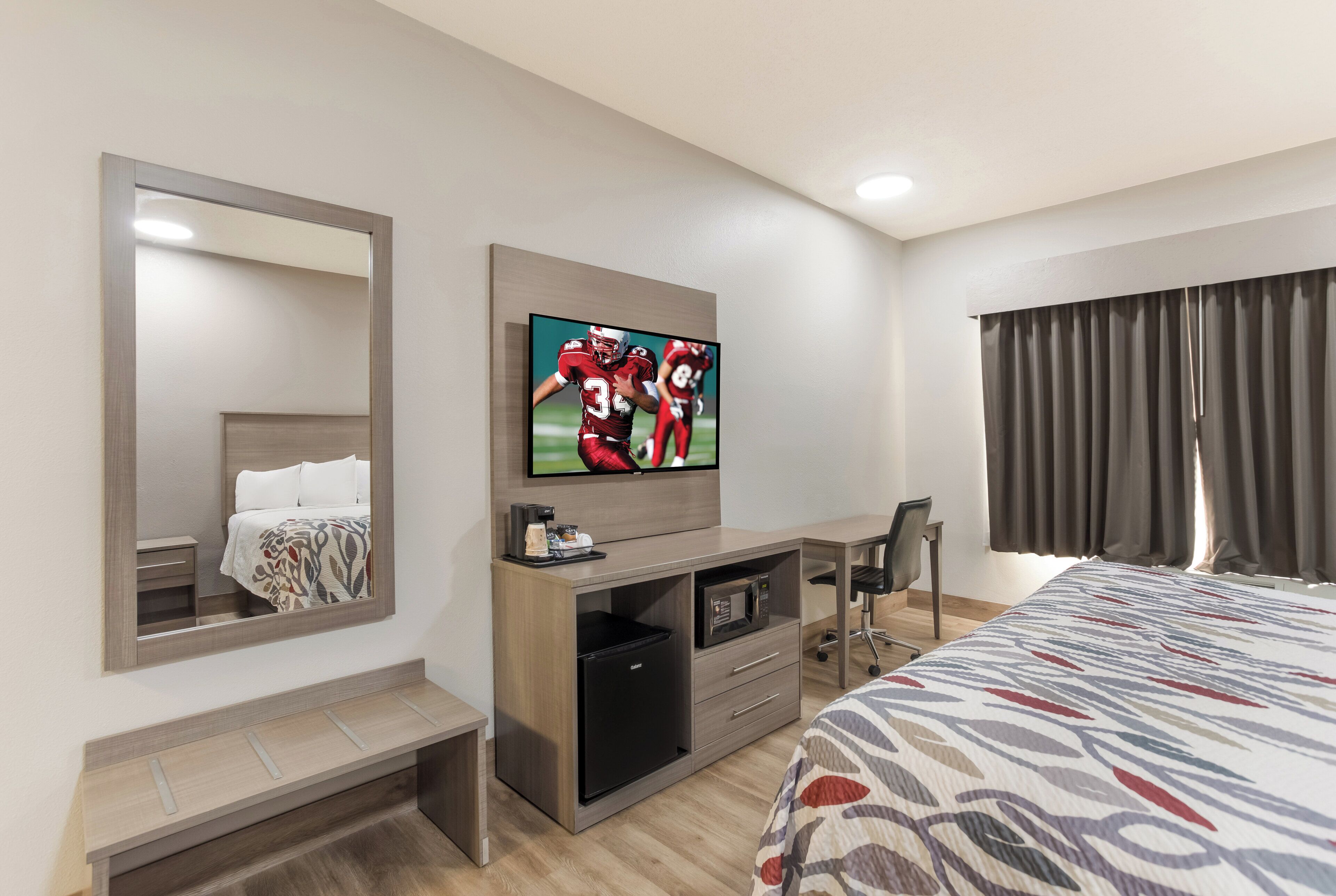 A hotel room with a bed, a desk with a flat-screen TV, a mirror, a coffee maker, and a microwave.