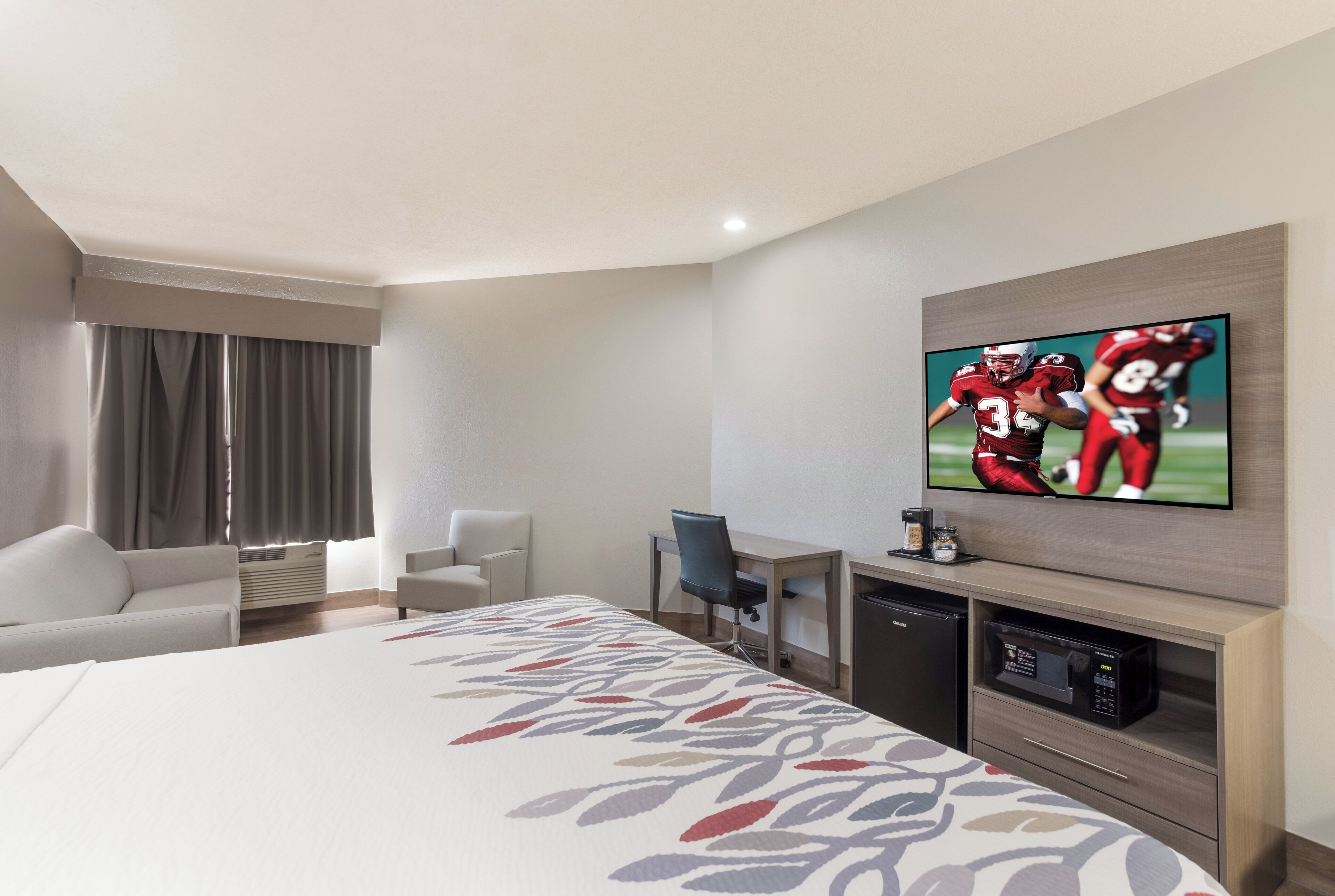 A hotel room with a bed, a desk, a chair, a television, and a minibar.