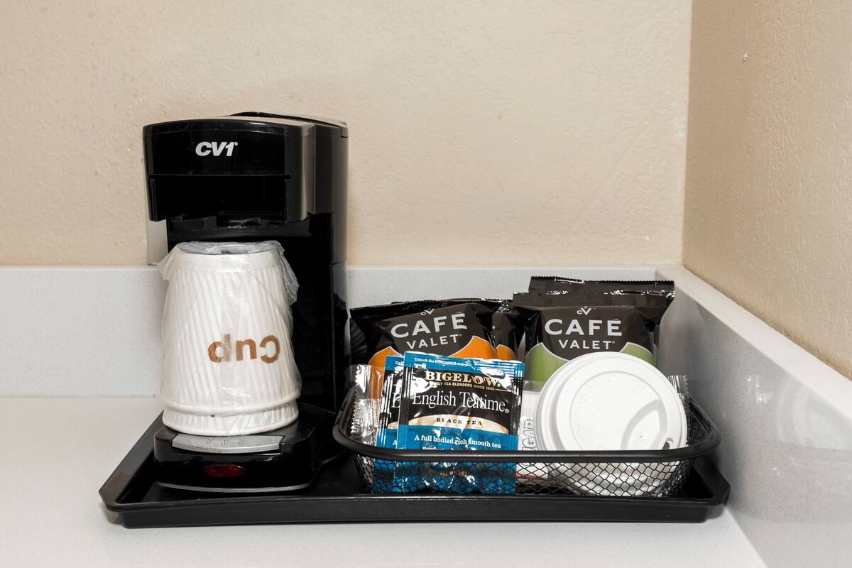 Una cafetera, una taza y bolsitas de té sobre una bandeja.