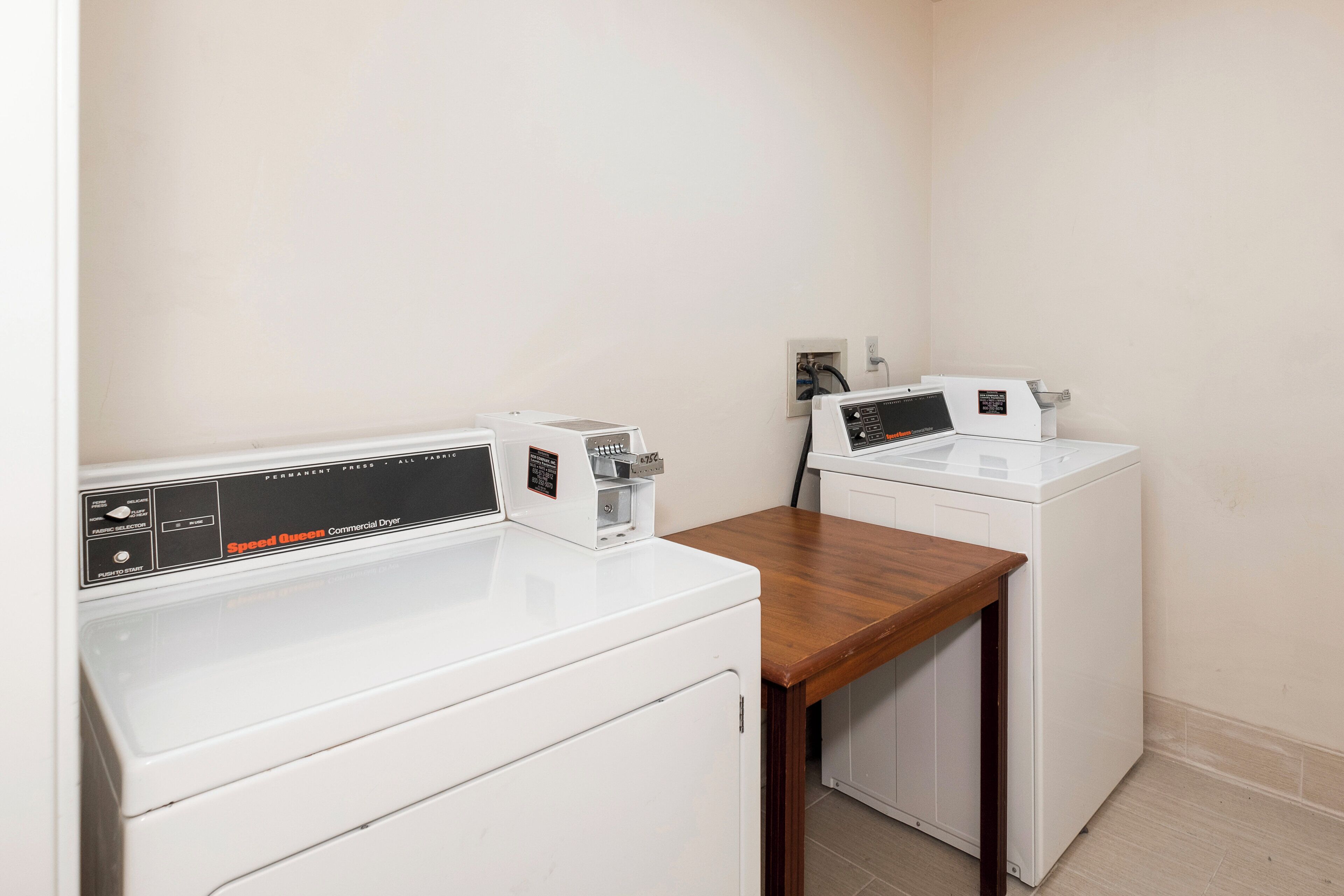 A laundry room with two white front-loading washing machines and a wooden table.