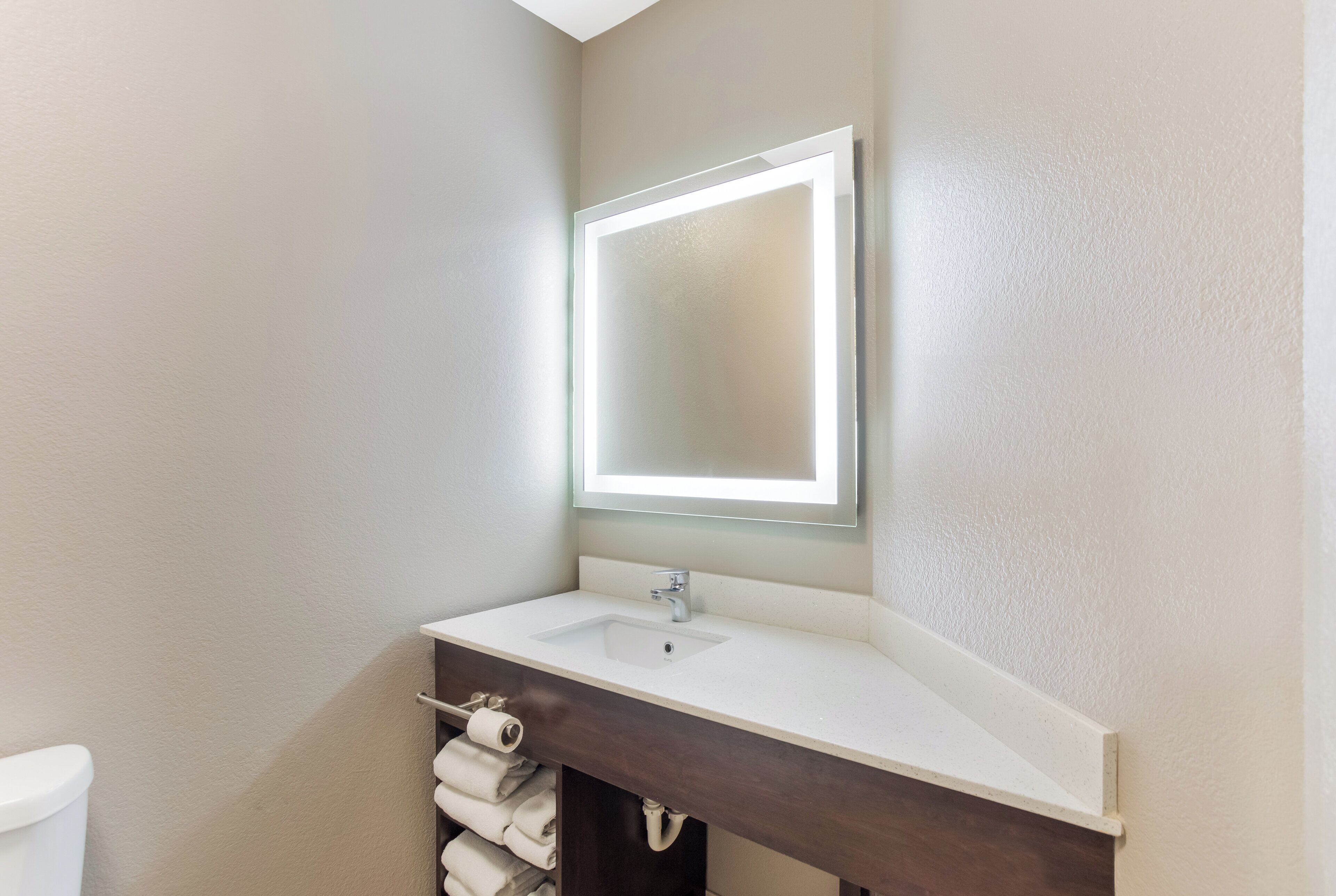 A bathroom with a white sink, a mirror with a light, and a towel rack.