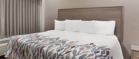 Une chambre d’hôtel avec un grand lit, une tête de lit et une fenêtre avec des rideaux.