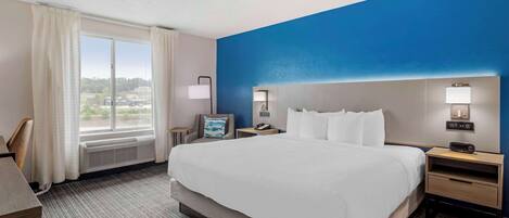 A hotel room with a large bed, two bedside tables, a desk, and a window with curtains.