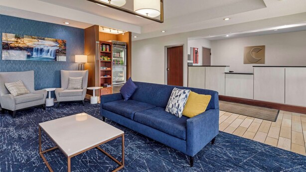 Un vestíbulo moderno con un sofá azul, dos sillones, una mesa de centro, una estantería y un refrigerador.
