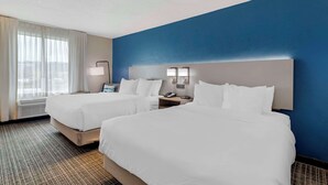 Una habitación de hotel con dos camas, una mesita de noche con lámpara y una ventana con cortinas.