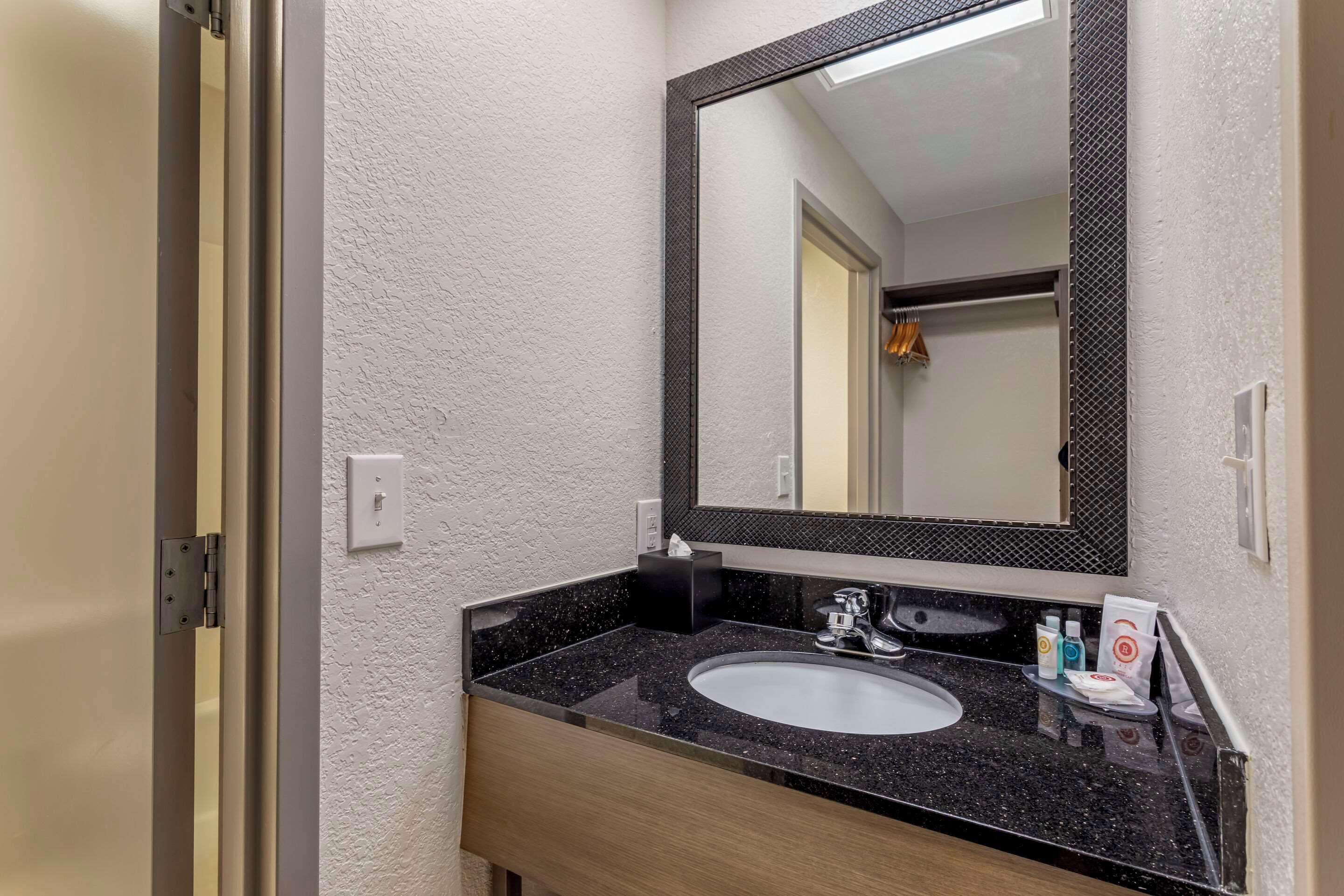 A bathroom with a black granite countertop, a white sink, and a large mirror with a black frame.