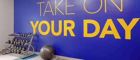 A gym with a motivational wall saying "TAKE ON YOUR DAY" and exercise equipment.