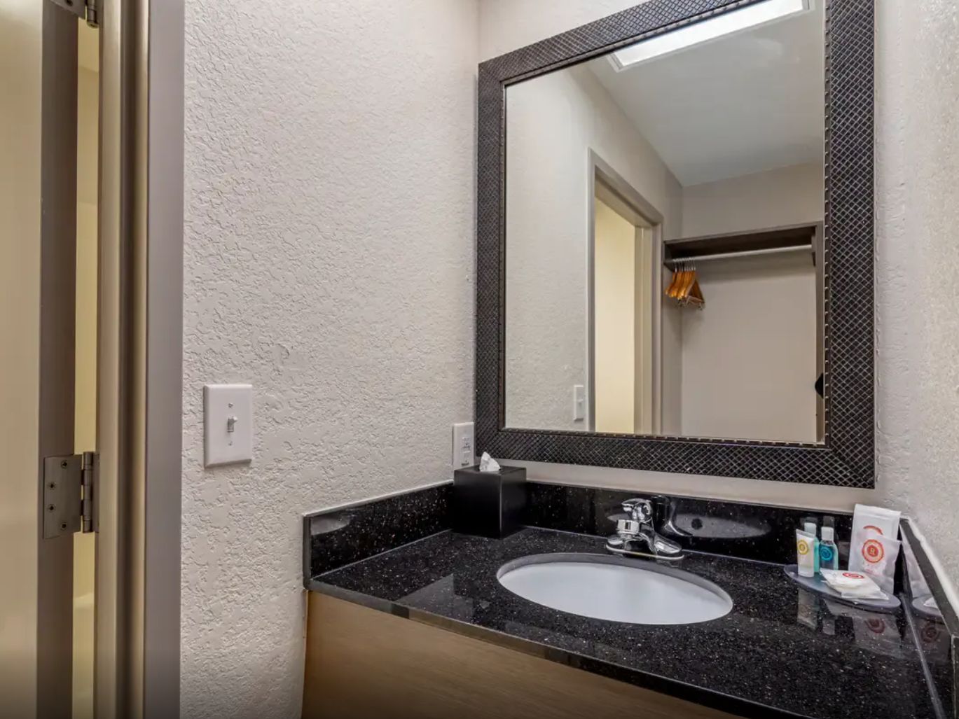 A bathroom with a granite countertop sink, a mirror, and toiletries.