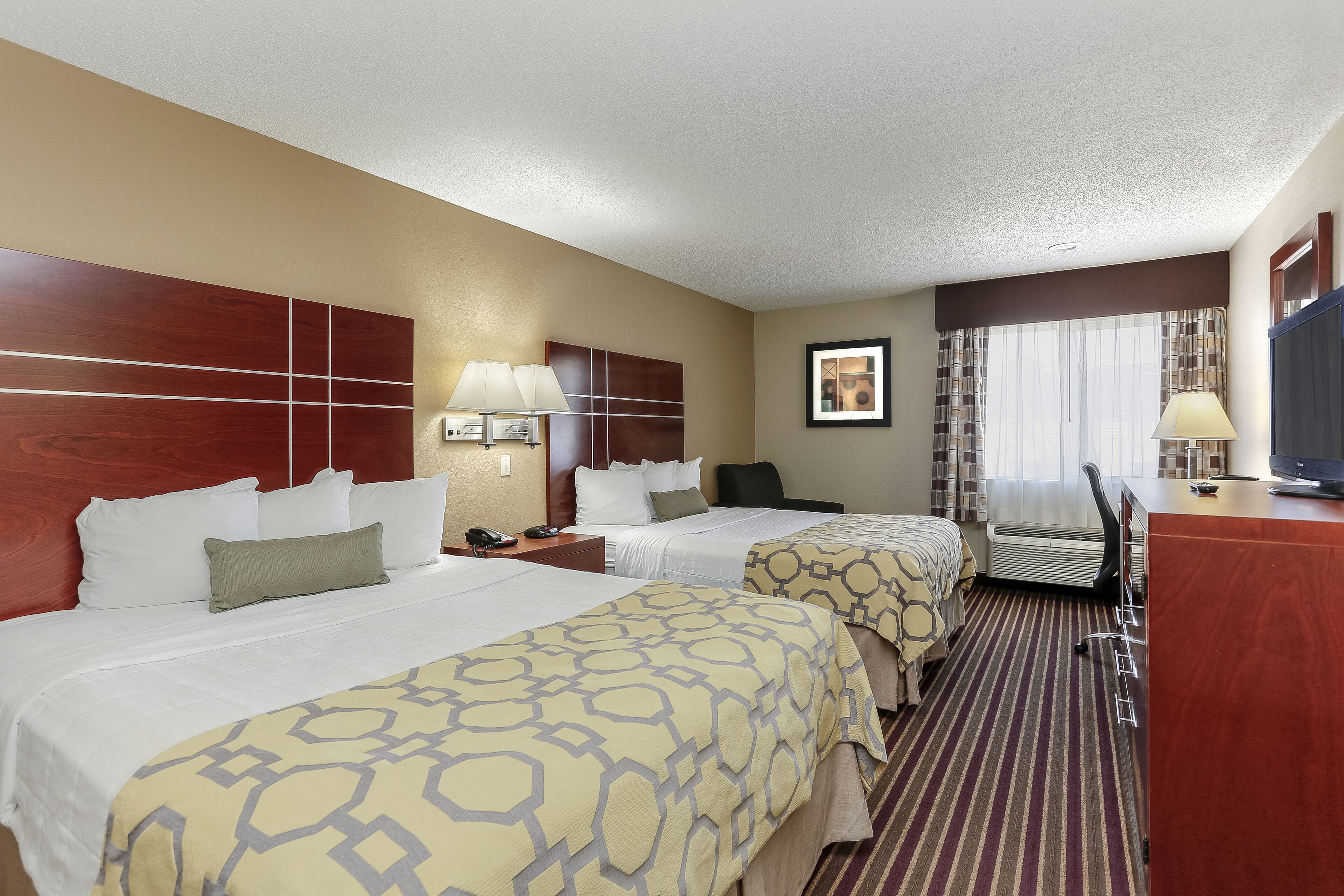 A hotel room with two beds, a desk, a chair, a TV, and a window with curtains.