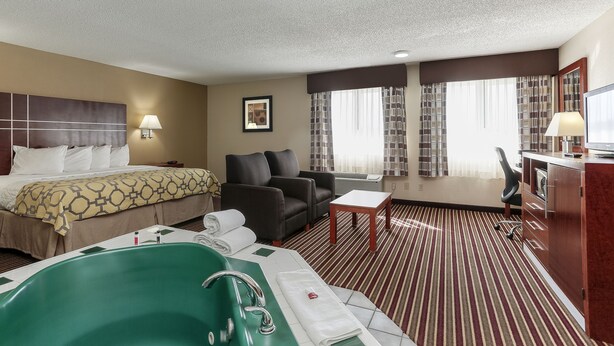 Una habitación de hotel con cama, una bañera verde, sofá, escritorio y un ventanal con cortinas.