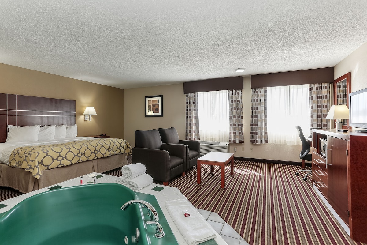 Une chambre d’hôtel avec un lit, une baignoire verte, un canapé, un bureau et une grande fenêtre avec des rideaux.