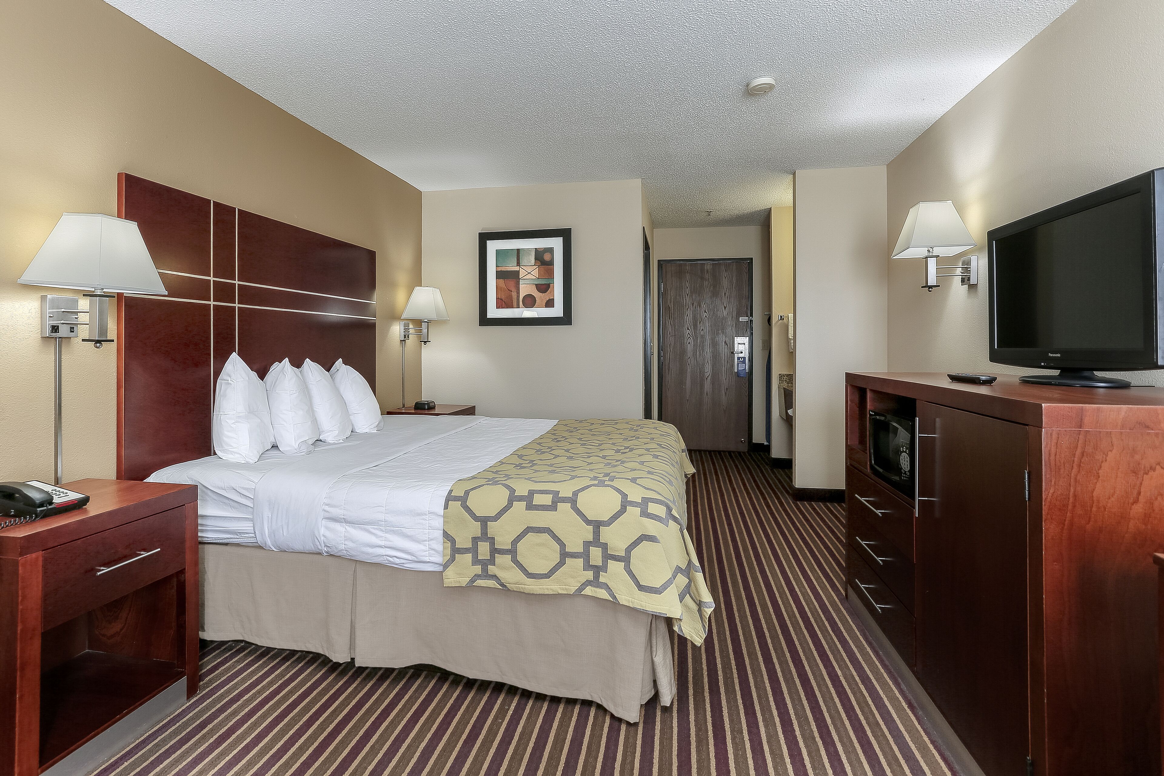 A hotel room with a bed, bedside tables, a TV, and a desk.