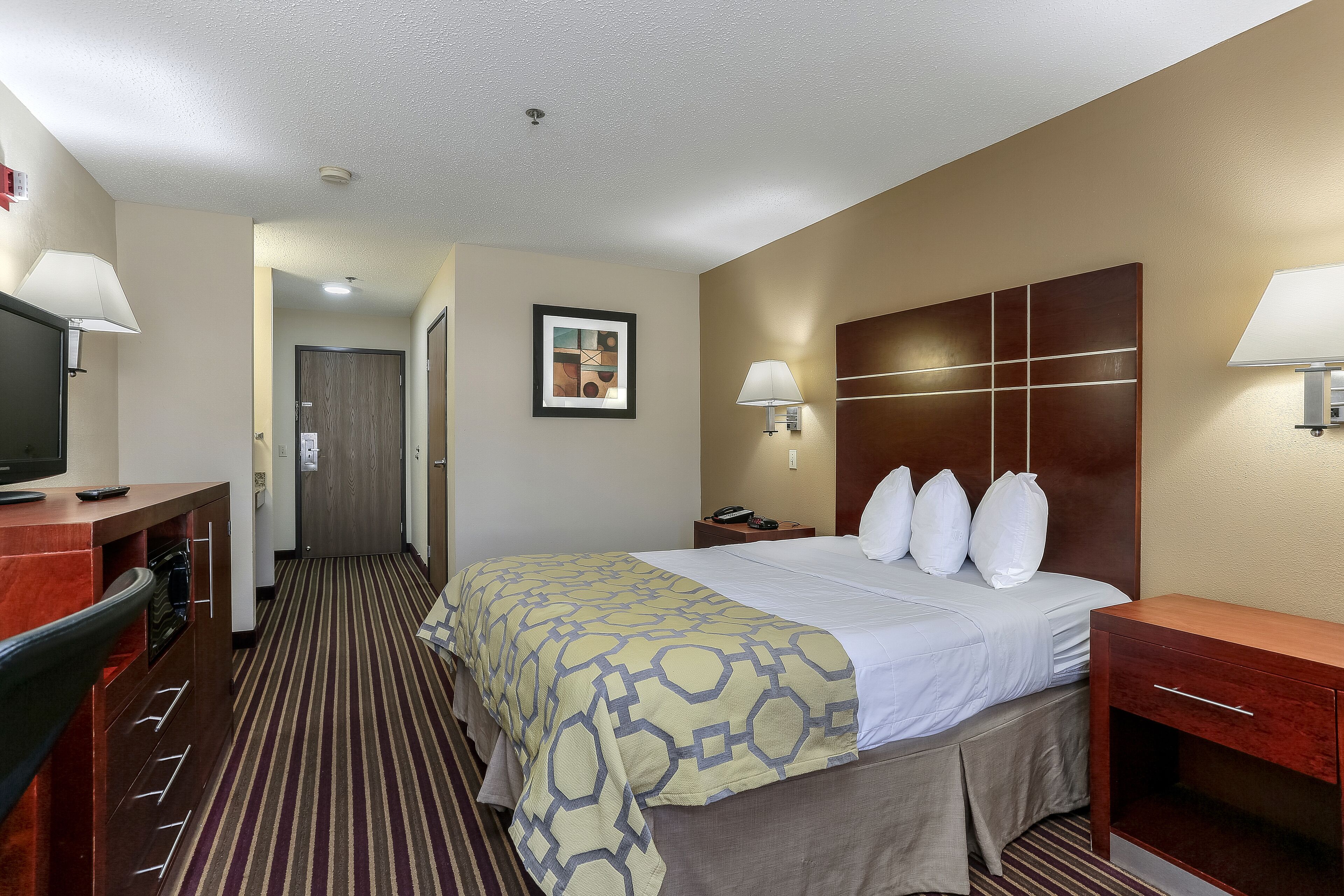 A hotel room with a bed, bedside tables, a desk with a TV, and a framed picture on the wall.