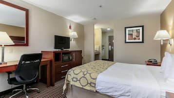 Habitación de hotel con cama, escritorio, silla, televisor y baño visible a través de una puerta abierta.