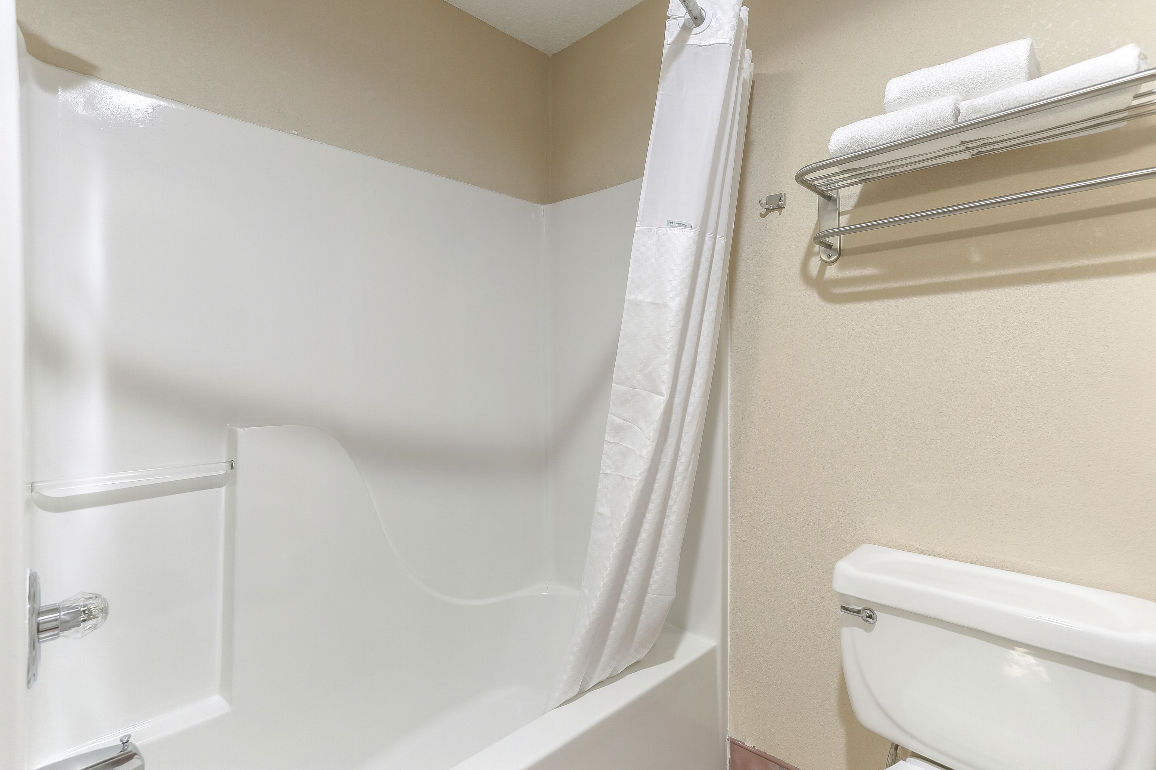 A bathroom with a bathtub, a shower curtain, a toilet, and a towel rack.