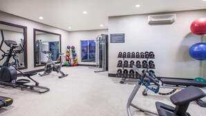 Un gimnasio con máquinas de cardio, equipo de levantamiento de pesas y un estante de mancuernas fijado a la pared.