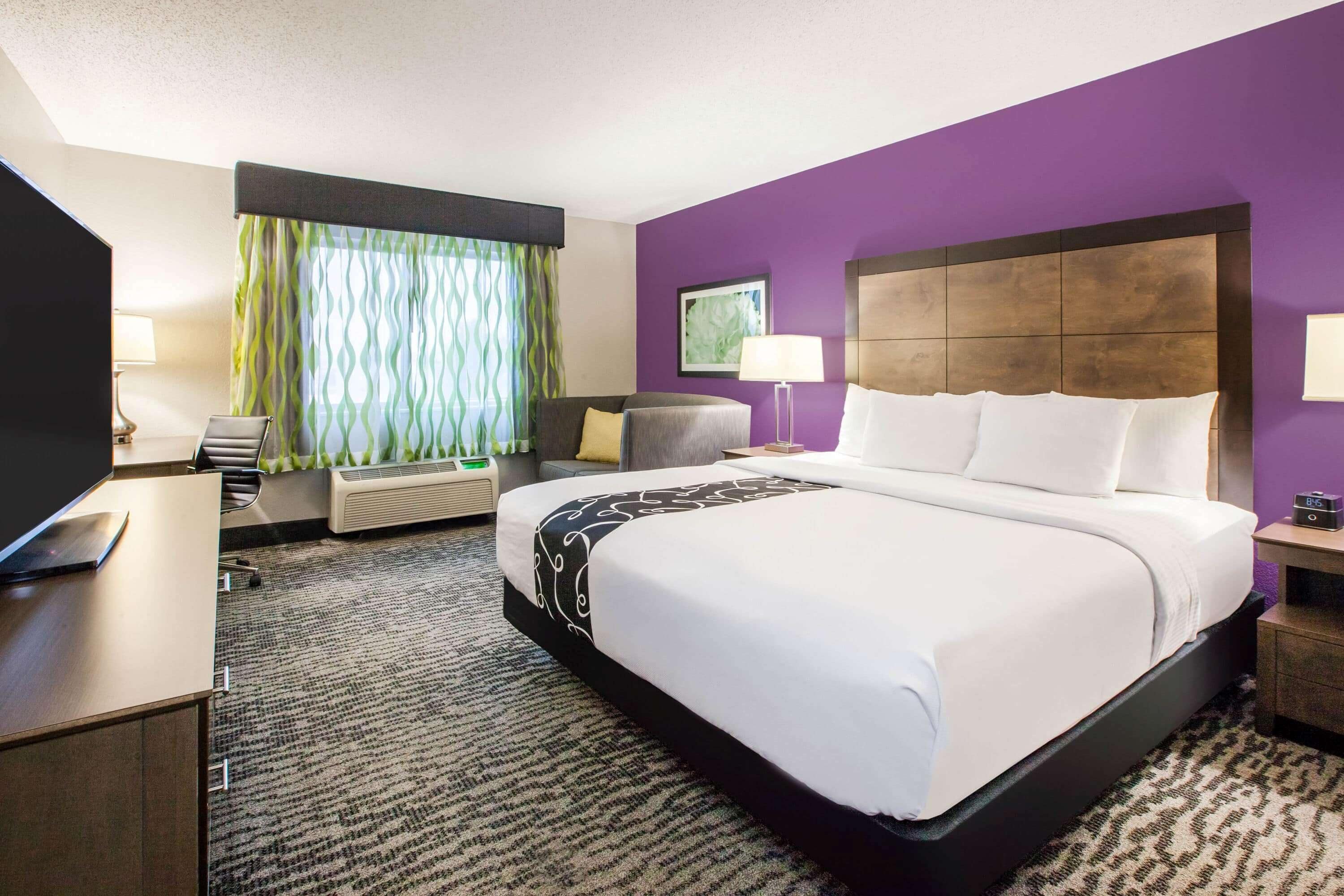 A hotel room with a large bed, a desk, a chair, a TV, and a window with curtains.