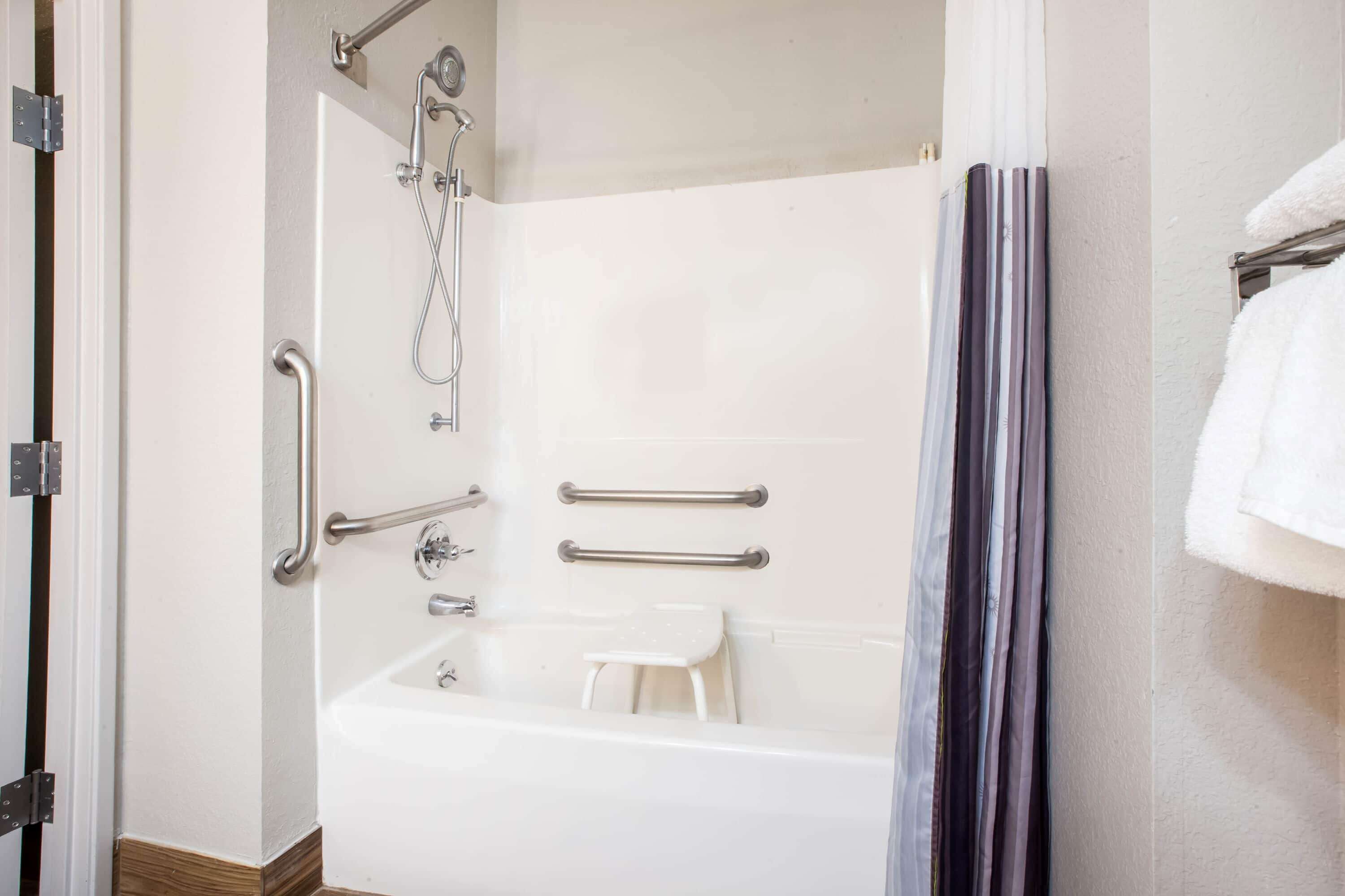 A bathroom with a white bathtub, grab bars, a showerhead, and a towel rack.