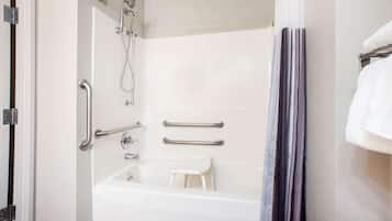 A bathroom with a white bathtub, grab bars, a showerhead, and a towel rack.