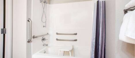 A bathroom with a white bathtub, grab bars, a showerhead, and a towel rack.