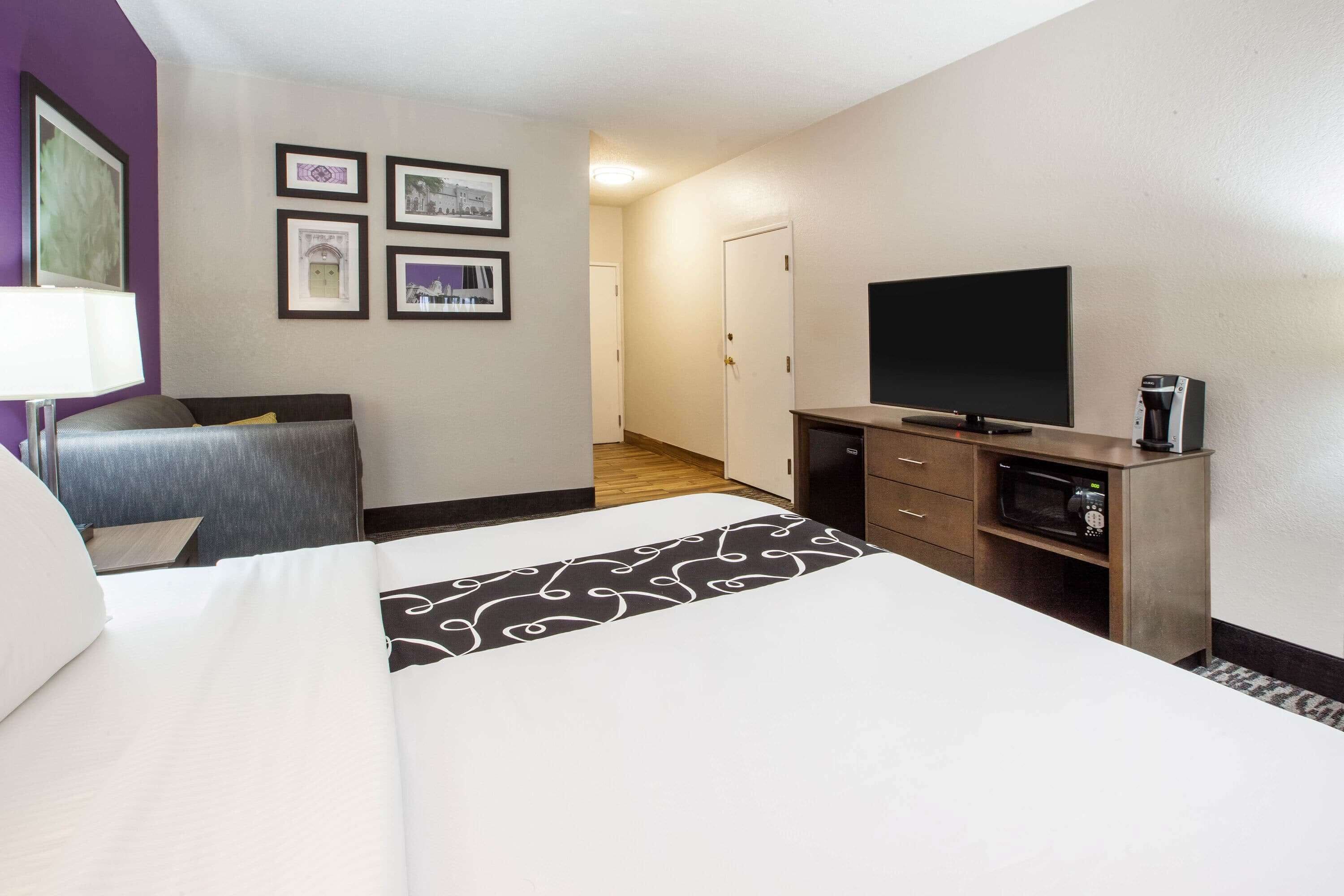 A hotel room with a bed, a TV, a coffee maker, and framed pictures on the wall.