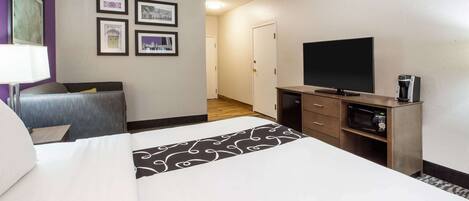 A hotel room with a bed, a TV, a coffee maker, and framed pictures on the wall.