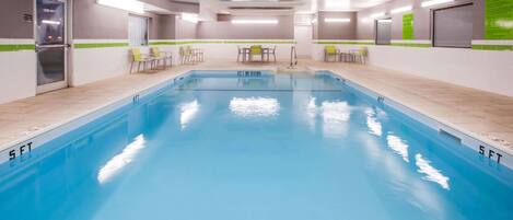 A swimming pool with a tiled edge, a door labeled "EXIT," and a table with chairs in the background.