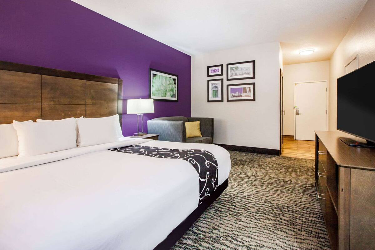 Una habitación de hotel con una cama grande, un escritorio, una silla, un televisor y cuadros en la pared.