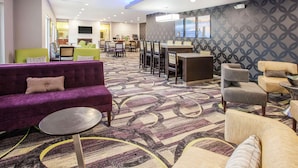 Un vestíbulo de hotel con un sofá morado, una mesa redonda y una zona de bar.