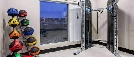 A gym with a pull-up bar, a rack of medicine balls, and a window with a view of a parking lot.
