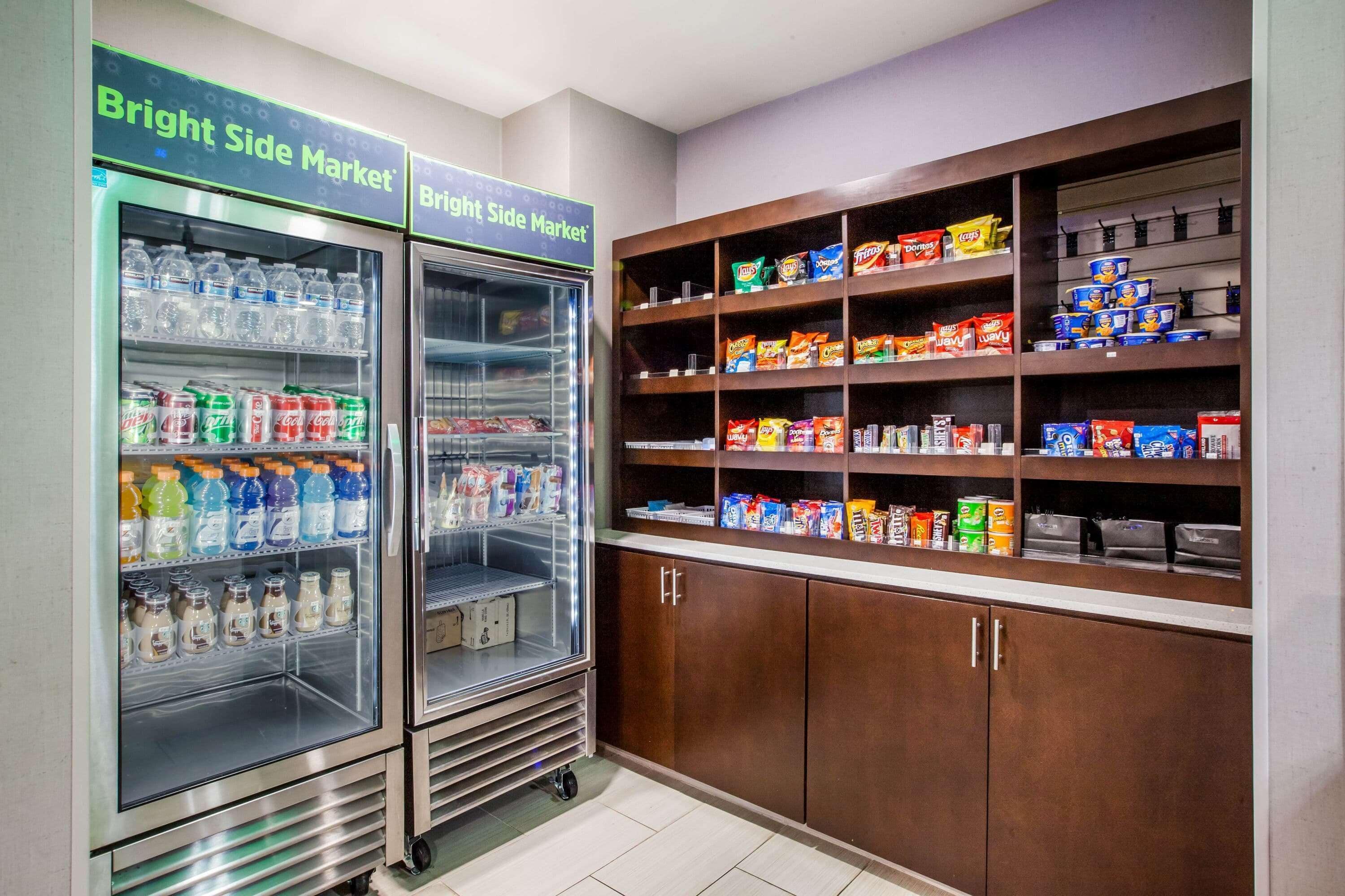 Un mercado luminoso con dispensadores de bebidas refrigeradas y estantes llenos de bocadillos y bebidas.