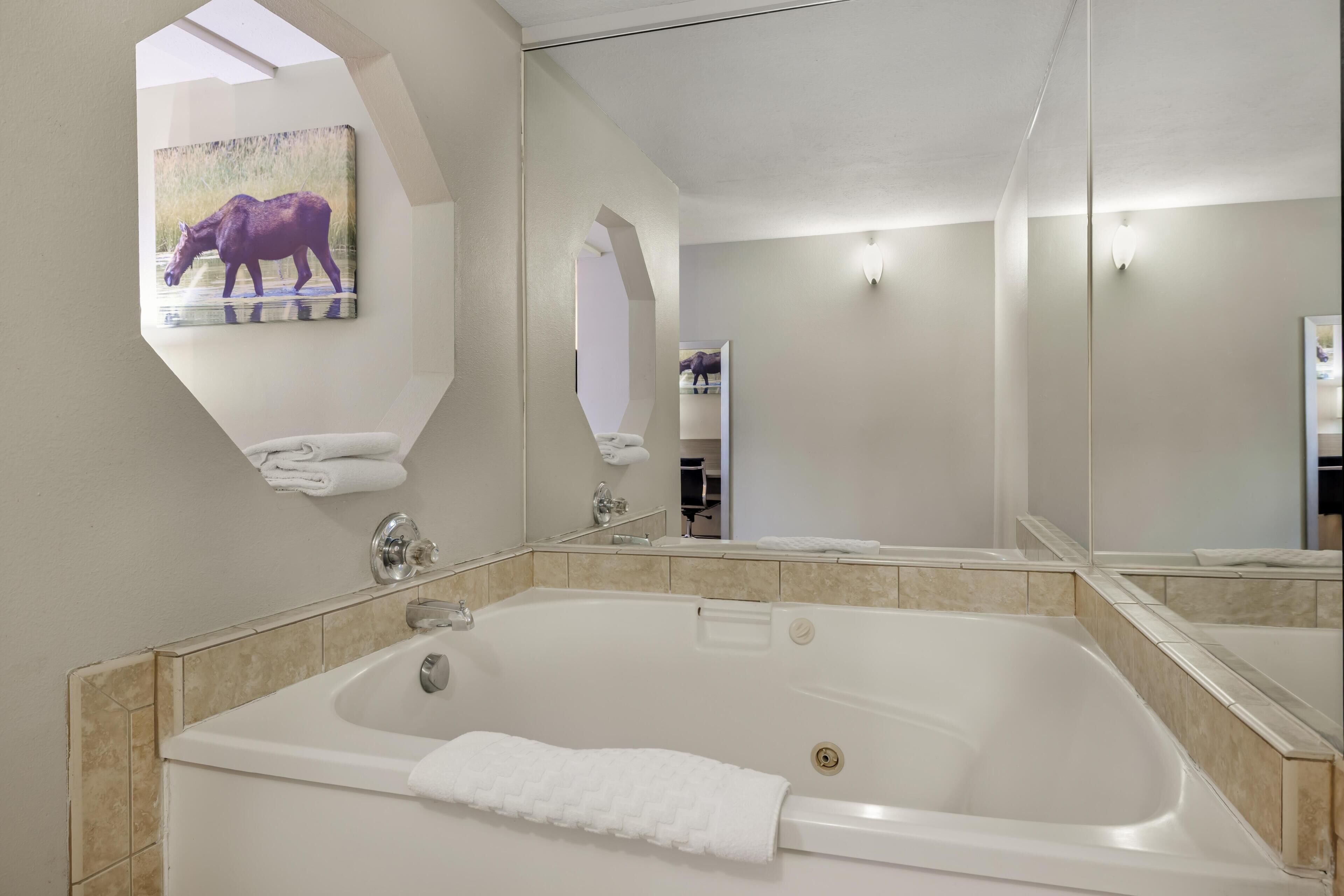Une salle de bain avec une grande baignoire, un miroir et un tableau représentant un élan, accroché au mur.