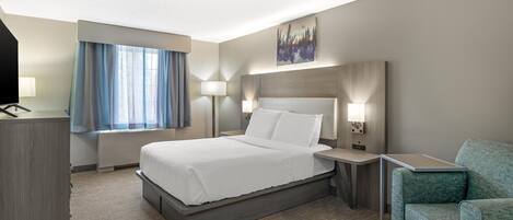 Quarto de hotel com cama, mesas de cabeceira, escrivaninha, cadeira, janela com cortinas e um quadro na parede.