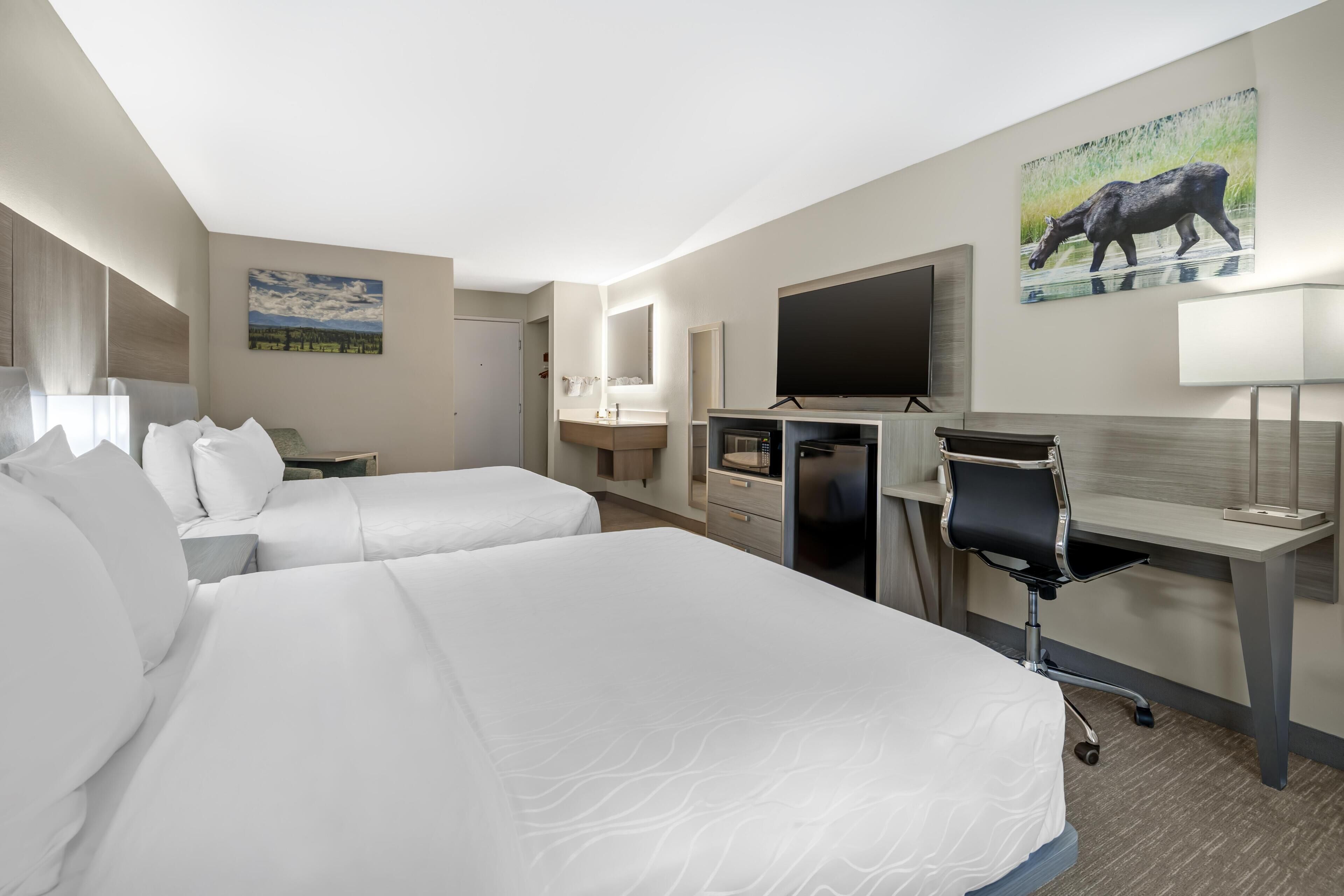 A hotel room with two beds, a desk, a chair, a TV, a mirror, and artwork on the walls.