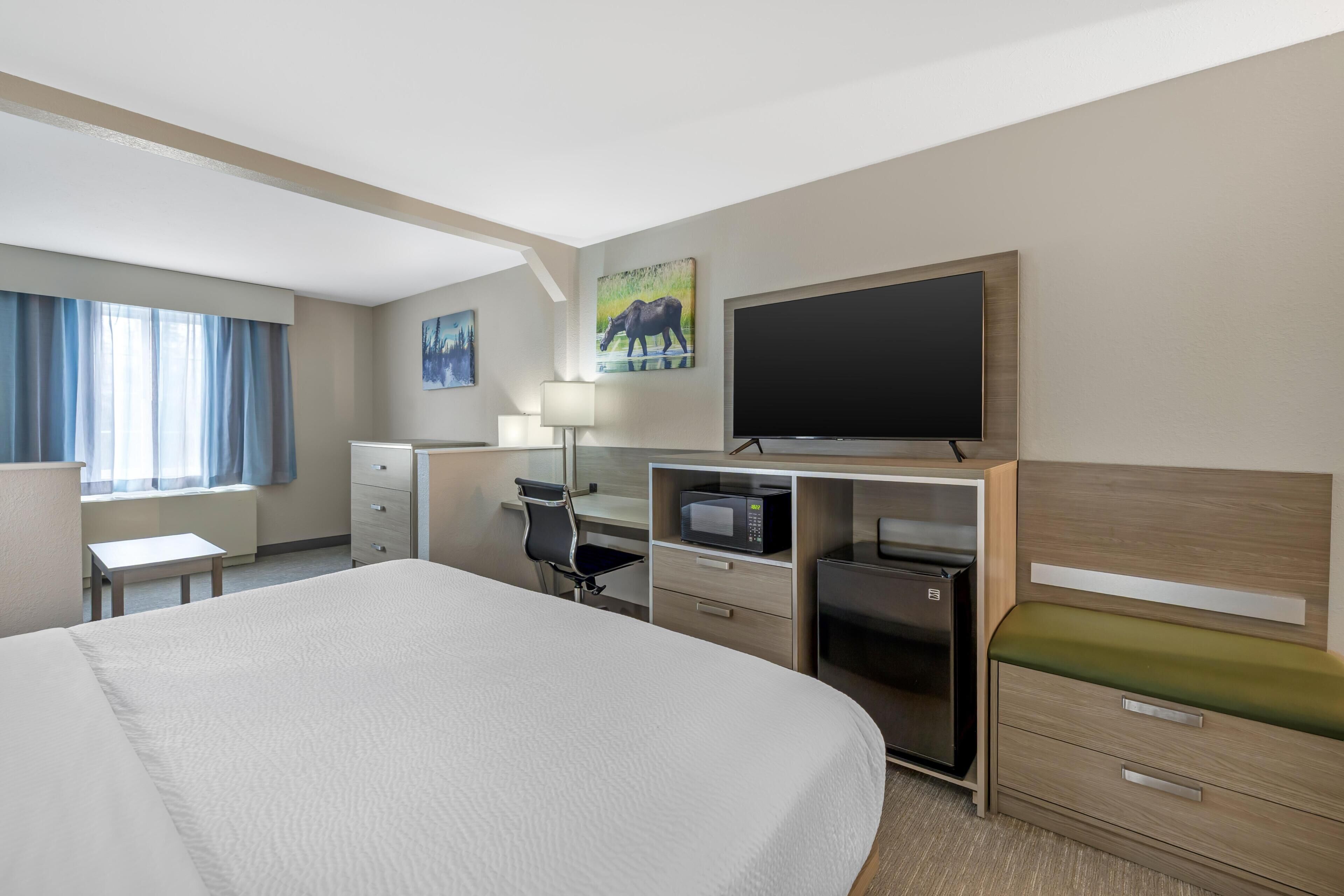 Ein Hotelzimmer mit einem großen Bett, einem Schreibtisch mit Computer, einem Flachbildfernseher, einer Mikrowelle und einem kleinen Kühlschrank.