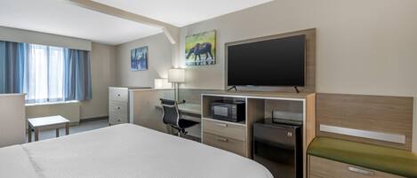 A hotel room with a large bed, a desk with a computer, a flat-screen TV, a microwave, and a small refrigerator.