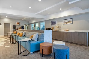 Ein moderner Wohnbereich mit einer Couch, Poufs und einer Küche im Hintergrund.