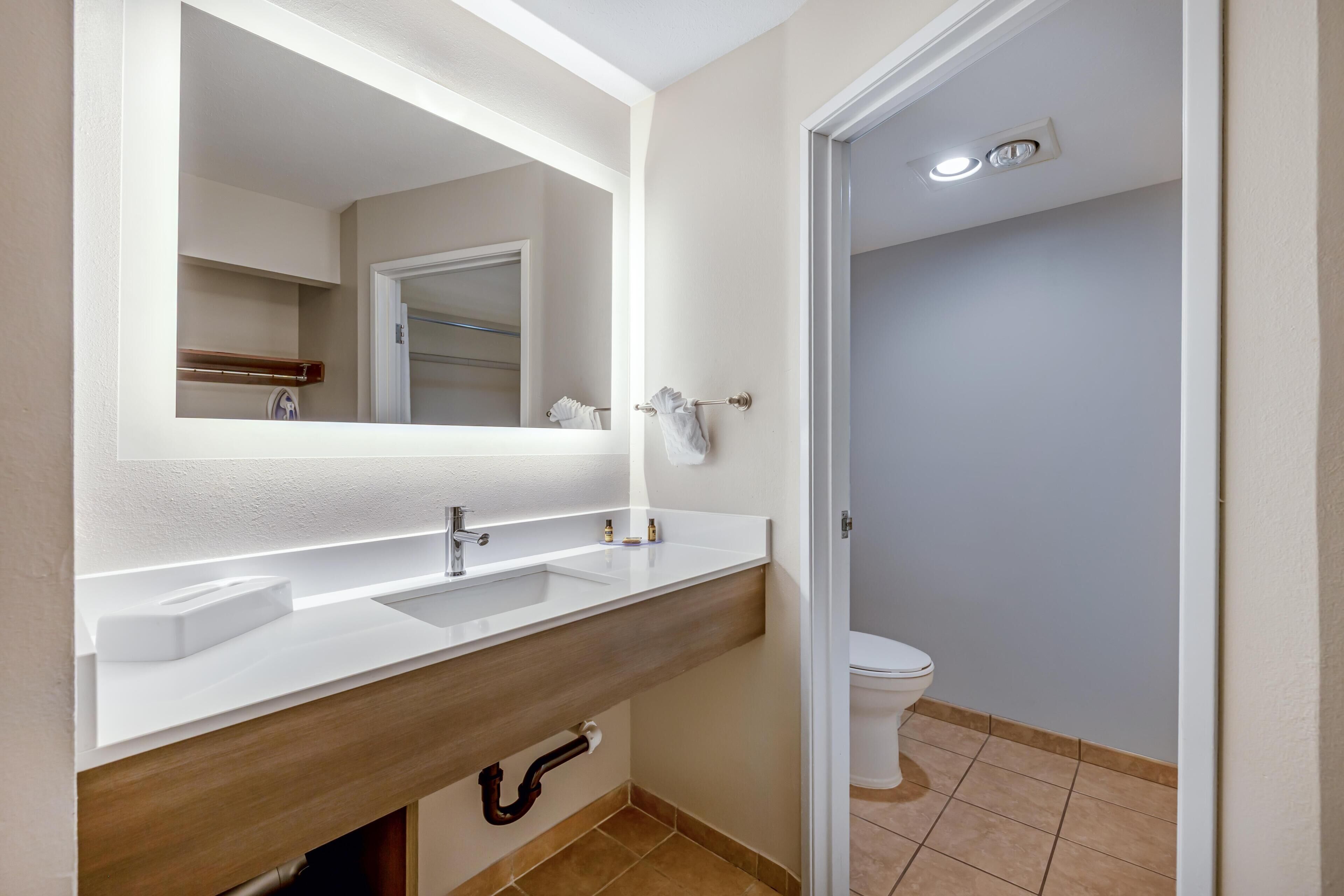 Un baño con tocador blanco, espejo, toallero y retrete.
