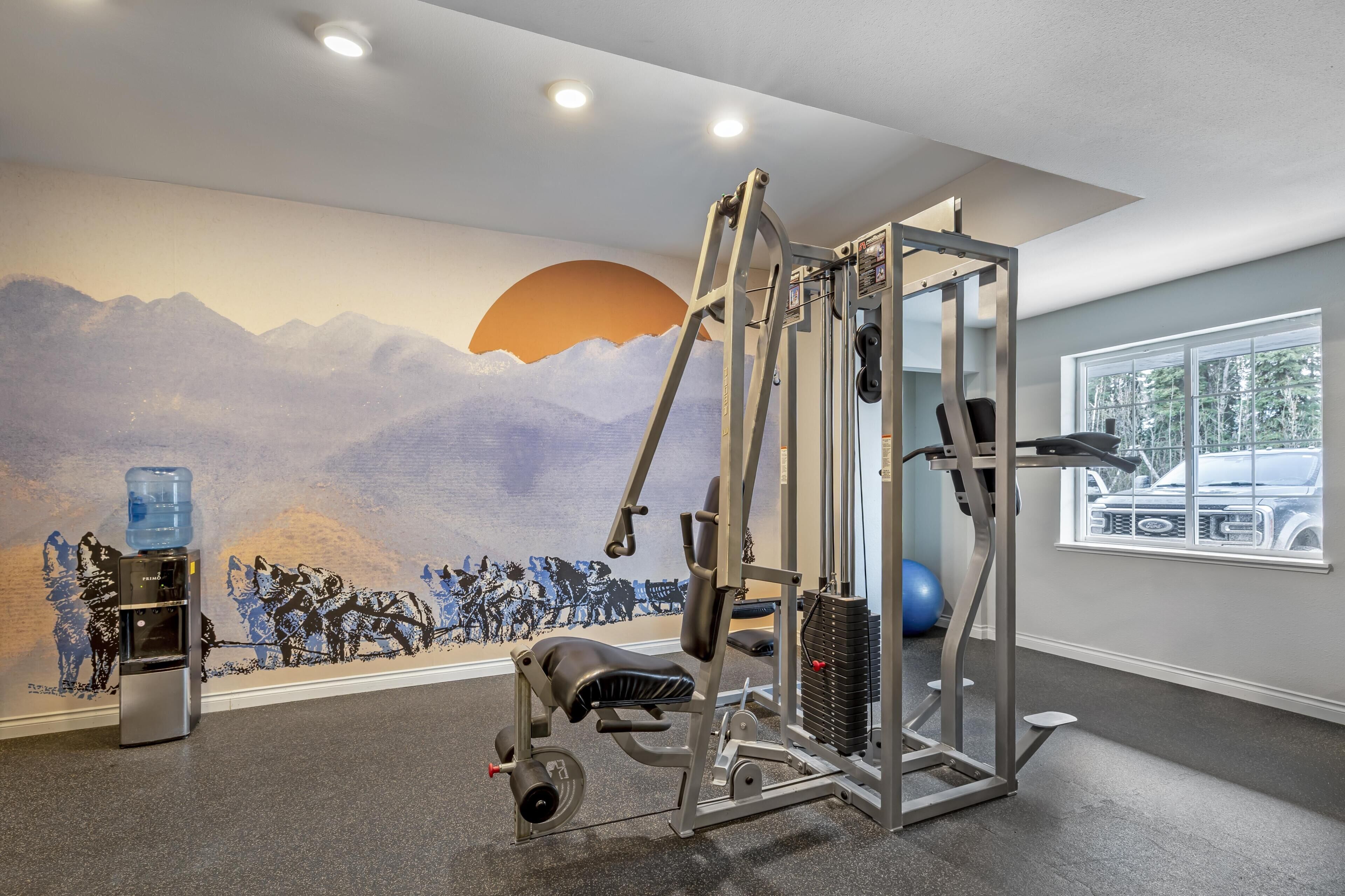A gym with exercise equipment, a water dispenser, and a mural of mountains.