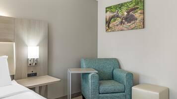 A hotel room with a bed, a desk, a chair, a bedside table, a wall-mounted lamp, and a painting of moose.