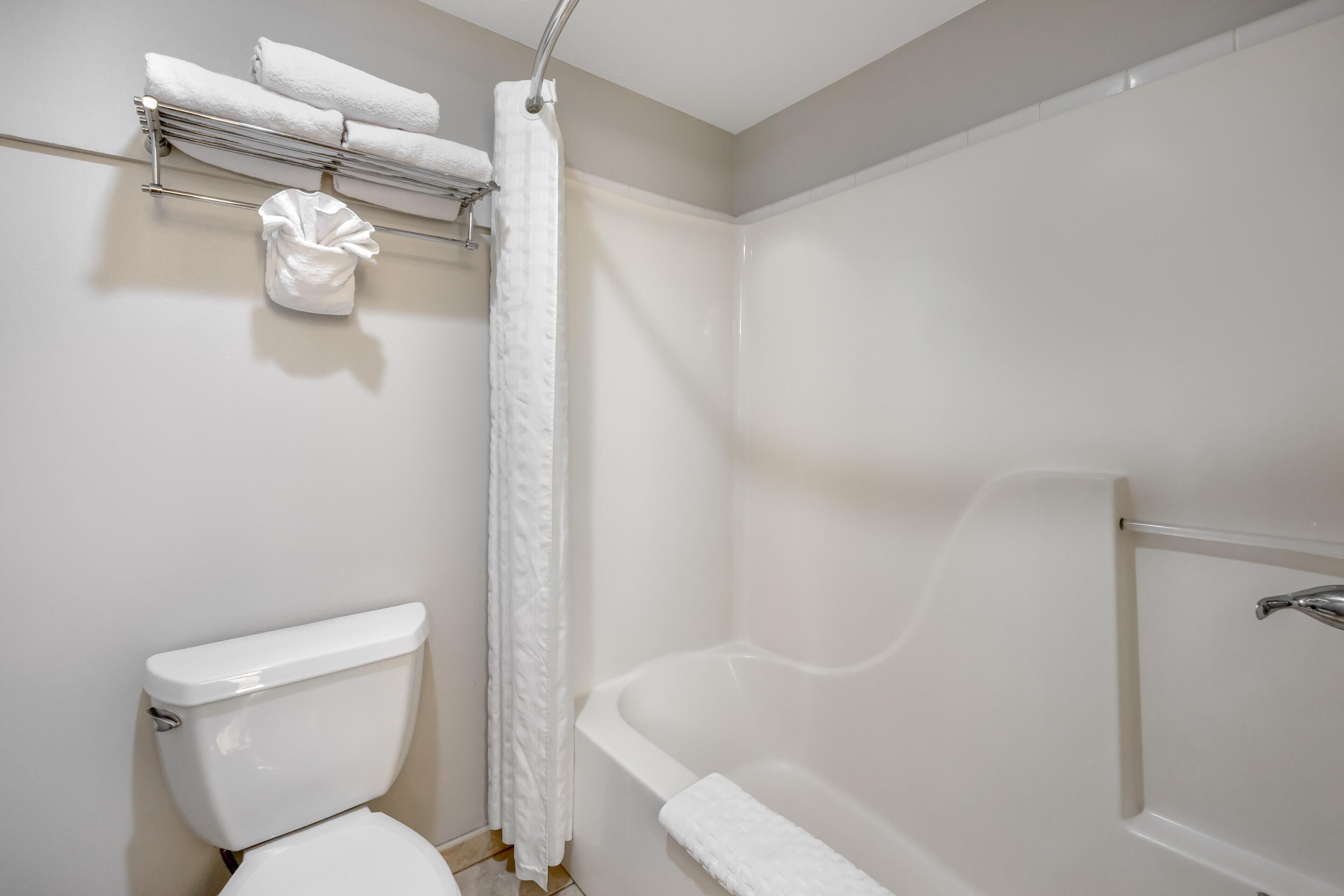 A bathroom with a toilet, a shower with a curtain, and a towel rack with towels.