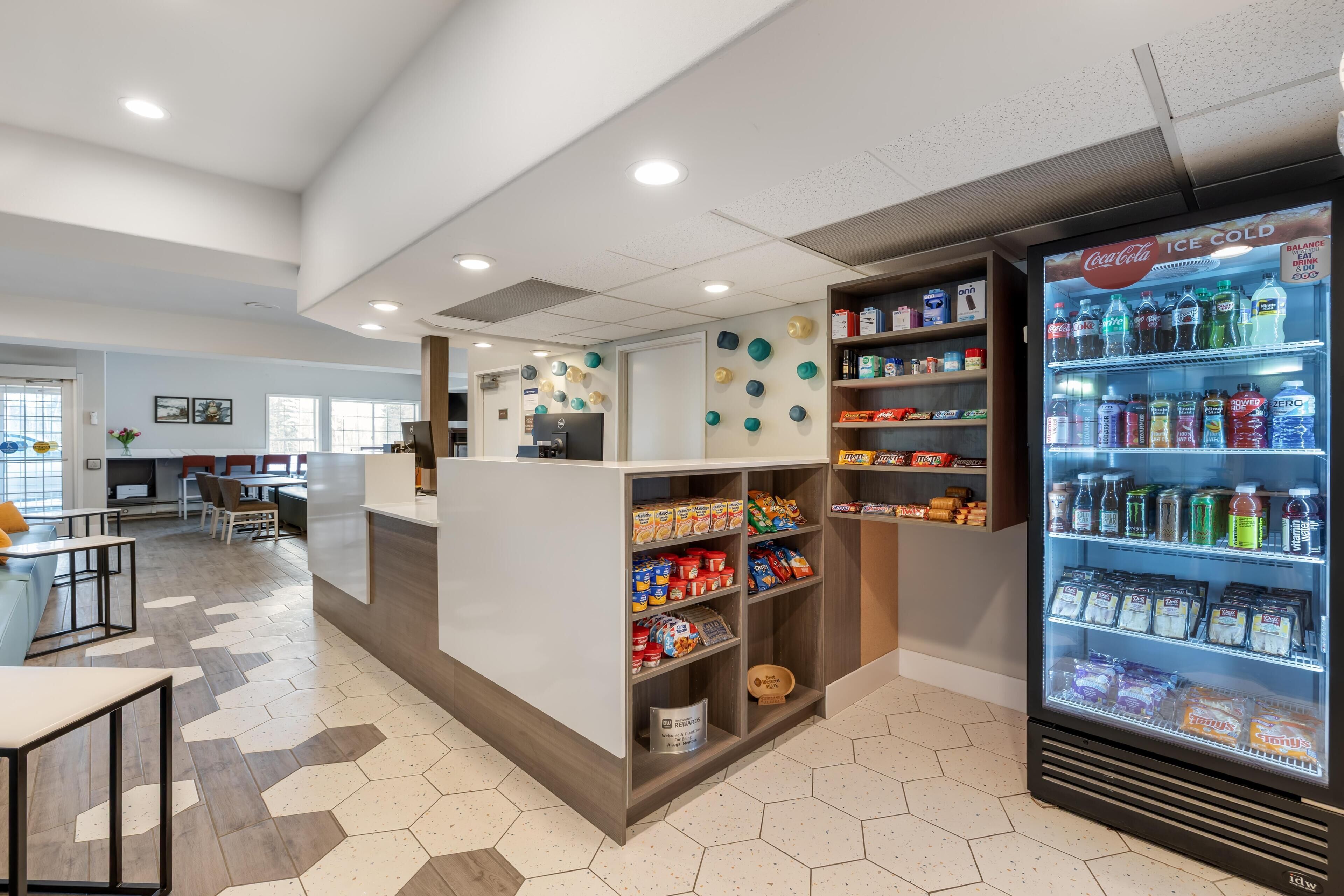 Un moderno vestíbulo de hotel con un mostrador de recepción, una zona de estar y un refrigerador Coca-Cola Ice Cold lleno de bebidas.