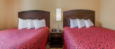 A hotel room with two beds, each with a headboard, a bedside table, and a lamp.