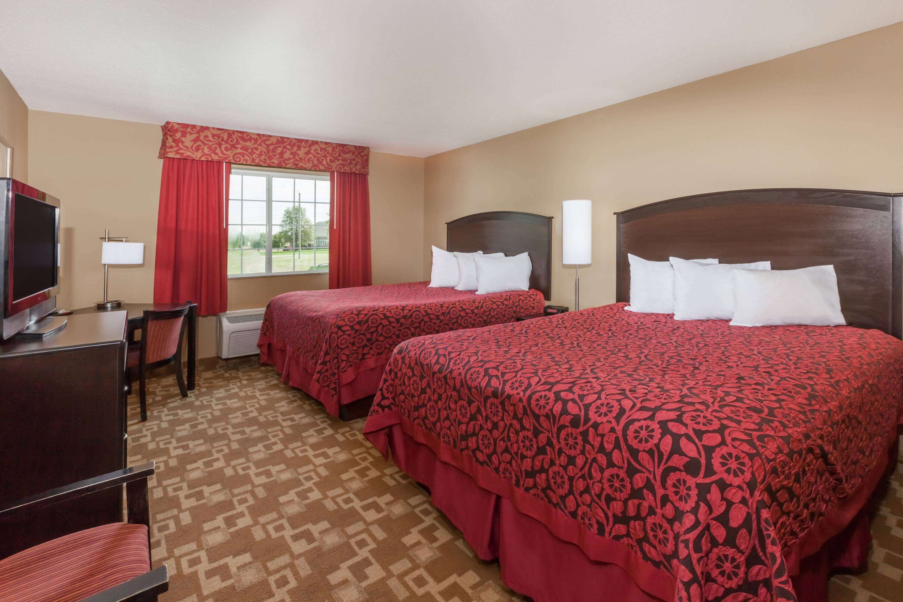 A hotel room with two beds, a desk, a TV, and a window with red curtains.